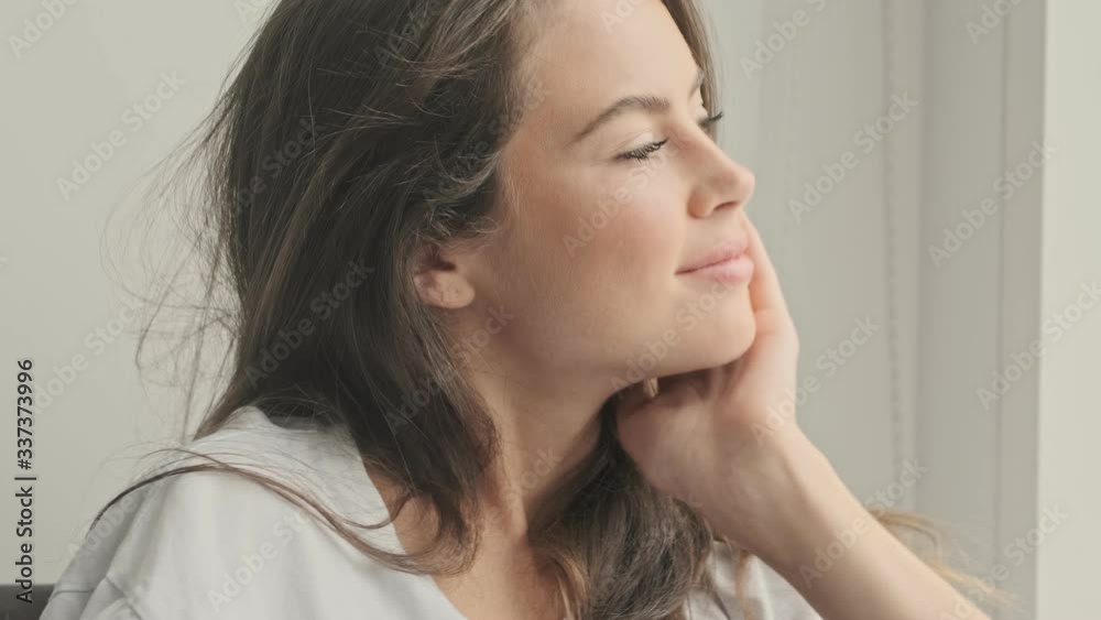 Sticker pleased pretty brunette woman touching her hair and looking away while sitting with apple on sofa at