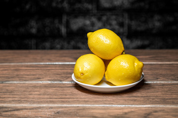 limones amarillos en un bol de color blanco sobre una madera y fondo oscuro