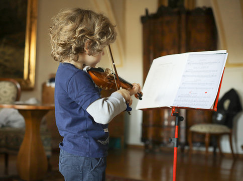 A little boy plays the violin at home. The child learns music.