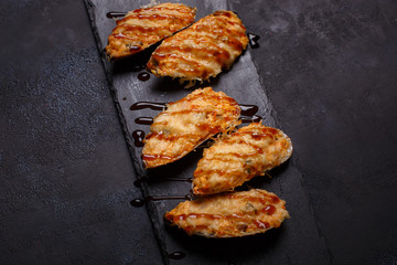 Delicious cooked mussels with sauce on a black slate on the dark background, top view, vertical.