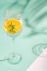 Summer homemade cold cocktail in a glass with lemon slice on a duotone background with leaf shadows.