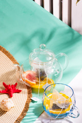 Fototapeta na wymiar Summer layout from wide-brimmed hat and glass set with ingredients for making fresh fruit cold tea drink on a duotone pastel background.