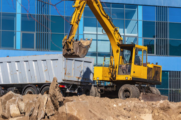 Obraz premium Excavator loader and dump truck during earthworks at a construction site. Loading land in the back of a heavy truck. Excavator digs land for the construction of a new park area.