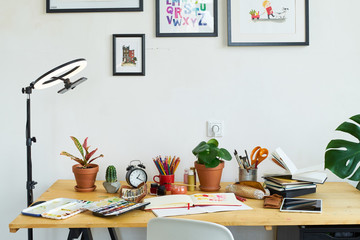 Artist's workplace for working from home with watercolor paints, brushes and sketchbooks. Place for design, illustration and creativity. Blogger ring light standing next to the table.