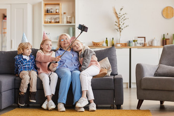 Grandchildren making selfie portrait together with their grandmother on the sofa at home