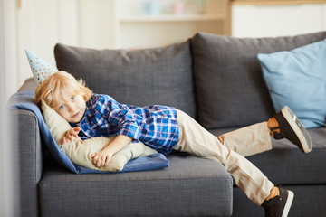 Portrait of little boy in casual clothing lying on sofa and resting in the living room at home