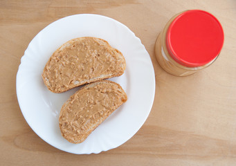Toast with peanut butter and a jar on a wooden table. Top view