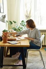 Fototapeta na wymiar Female artist at her workplace working from home. Woman dressed in jeans and striped shirt sitting at the table and drawing illustration.