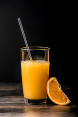 Orange juice is poured into a glass and a slice of orange on a black background