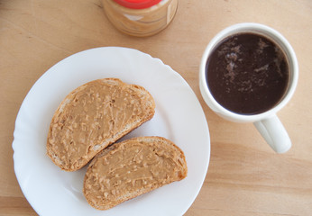 Peanut butter toasts on a white plate, a cup of coffee and jar on the wooden table. Top view