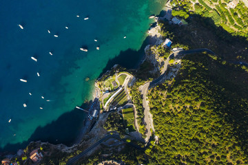 Naklejka na ściany i meble Aerial shot to the sea with boats and rocky green shore. Serpentine road along the mountains. South Italy. Beaautiful landscape. View from above.