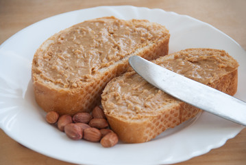 Peanut butter sandwiches or toasts, peanuts and knife on light wooden background