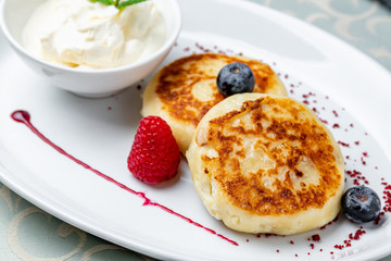 cheesecakes from cottage cheese on white plate with berries and sour cream