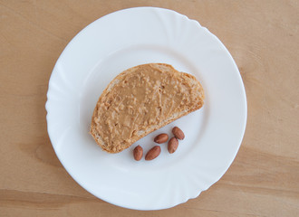Toast with peanut butter and peanuts on a white plate, view from above