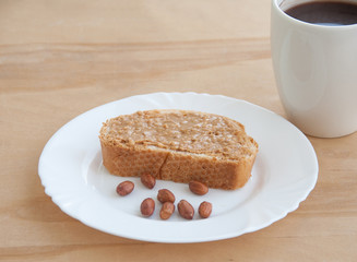 Peanut butter sandwich with peanuts on a white plate. A cup of coffee. Wooden table