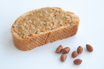 A slice of whole wheat bread with smooth peanut butter and peanuts isolated on white background