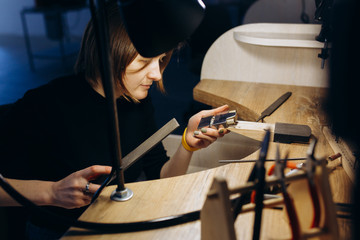 Back view of serious concentrated young European female designer with dark and short hair working on new collection of jewelry. Creating process