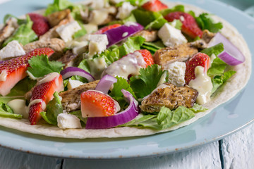 Open tortilla wrap with cold chicken salad, feta and strawberries - close up