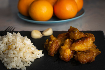 Chicken with orange sauce, rice, garlic on a slate board and bowl of oranges