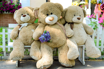 Three big teddy bears sit on chair in the garden. 