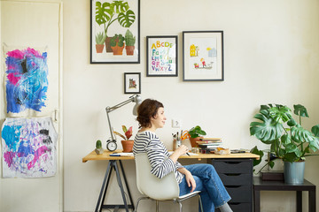Female artist at her workplace working from home. Young woman dressed in jeans and striped shirt...