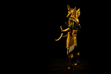 Obraz na płótnie Canvas a male actor in a suit of an Egyptian mythology character, the golden deity Jackal Anubis, twists buugeng in yellow light on a black background