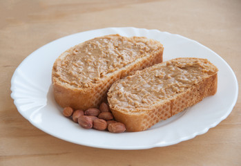 Peanut butter sandwich and peanuts on white plate. Wooden background. Close up