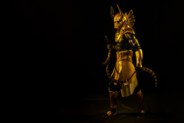 a male actor in a suit of an Egyptian mythology character, the golden deity Jackal Anubis, twists buugeng in yellow light on a black background