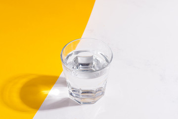 Top view of glass of fresh cold clean water on a duotone yellow white background with soft shadows and reflection.