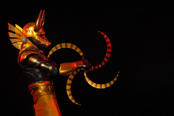 a male actor in a suit of an Egyptian mythology character, the golden deity Jackal Anubis, twists buugeng in red light on a black background