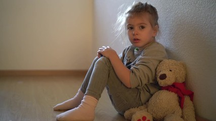  Sad child leaning to the wall by the window. Orphan girl is lonely. Child abuse concept.  Abandoned child.