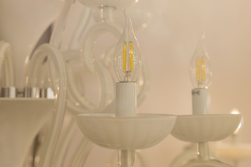 Close up on crystal of classic style lamp, is a branched ornamental light fixture designed to be mounted on ceilings. Soft warm filter, selective focus. Indoor. White glossy glass.
