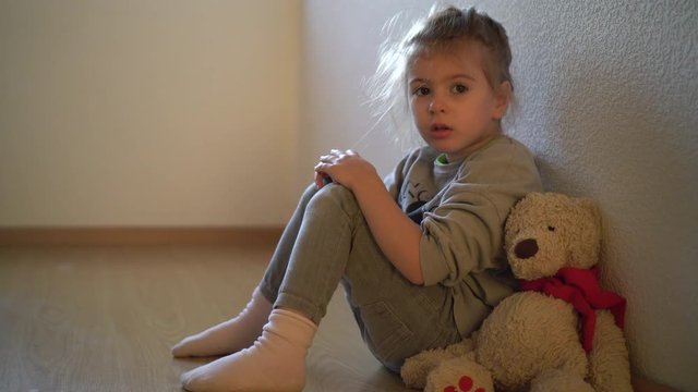  Sad child leaning to the wall by the window. Orphan girl is lonely. Child abuse concept.  Abandoned child.