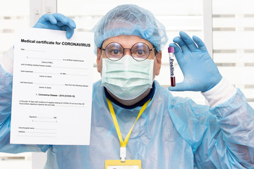 Doctor in protective suit holding medical certificate at coronavirus and tube with positive blood test results. The Laboratory examination of blood with a positive result for the disease corona virus.