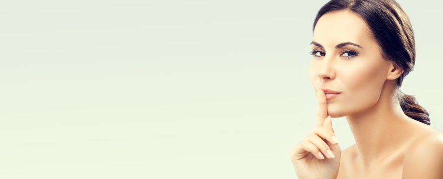 Portrait of beautiful young brunette woman keeping finger on her lips and asking to keep quiet, with copy space area, for some text, advertising or slogan