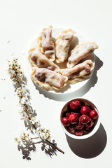 Cooked dumplings with cherries on white background. Vertical photo.