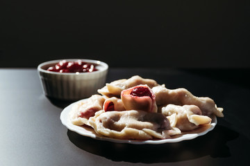 Dumplings with cherries on a black background. European cuisine, recipe.