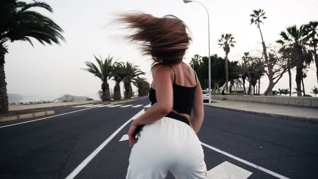 Sexy girl with beautiful body and big butt dancing twerk at the resort, tropical area. Rare view of a girl moves her butt standing on the asphalt. Brunette girl moves her body outdoors. Close up