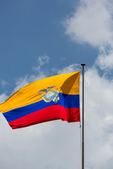 Large Ecuador flag waving in Quito Presidential Palace with a cloudy blue sky in the background.