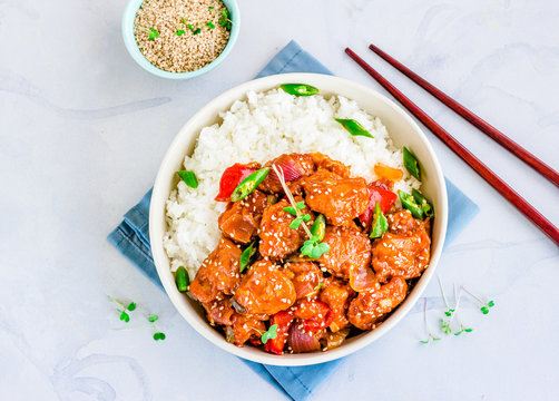 Stir fried fish with veggies on top of rice in bowl on white  background garnished with fresh micro greens