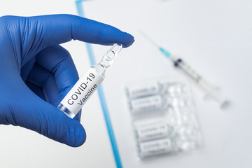 Naklejka premium Hand in medical glove holding ampoule with label Covid-19. coronavirus vaccine.