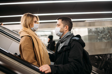 Side view of loving couple in medical masks on escalator in subway. Coronavirus pandemic.