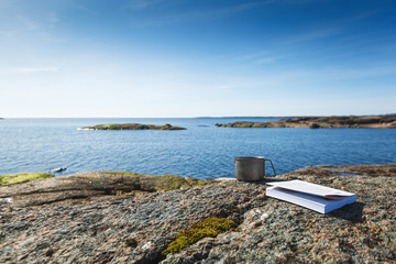 A mug with a book on a stone seashore. Cup in focus, blurred background.