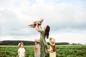 Beautiful young caucasian mother with children in a linen dress with a basket of strawberries gathers a new crop and has fun with the children © jul14ka