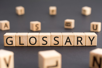 Glossary - word from wooden blocks with letters, alphabetical list of terms glossary concept, random letters around black background