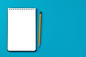 Notepad copy space and pencil on a blue background top view.