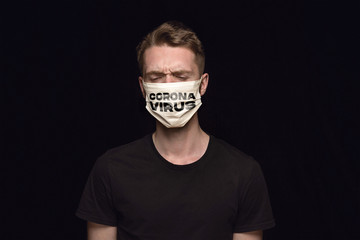 Sad man in protective mask with word CORONAVIRUS on black background. Prevention against pneumonia. Chinese coronavirus spreading, treatment. Healthcare, medicine, isolation, quarantine concept.