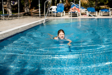 Girl child in swimsuit near pool, child jumps