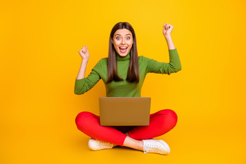 Photo of beautiful lady sit floor hold notebook read online table with examination results celebrate best grade mark wear green sweater red trousers isolated yellow color background