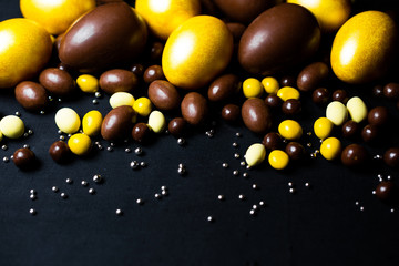 Golden eggs and delicious chocolate easter eggs and yellow sweets on black background